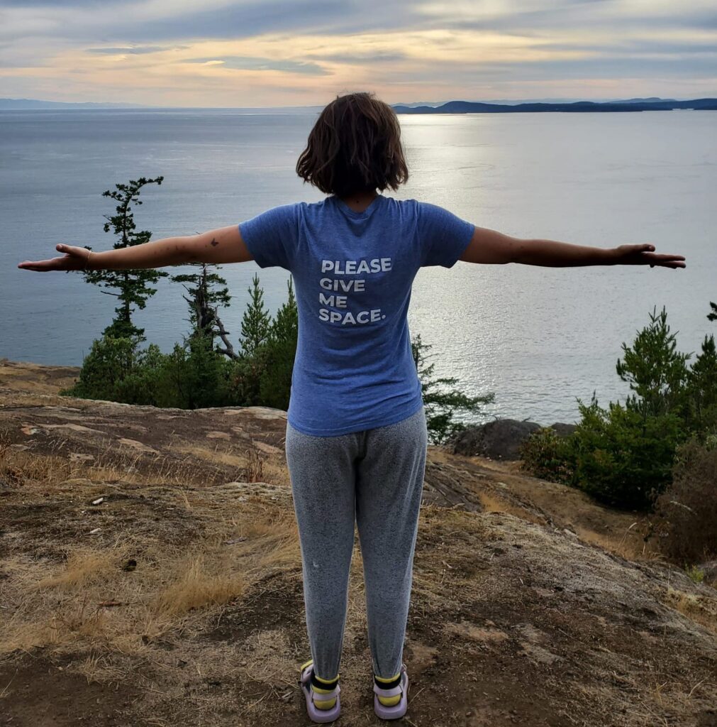 Emily Levy standing on the edge of a rock, wearing a blue t-shirt that says "Please Give Me Space." She is offering her top tips to advocate for yourself in healthcare.